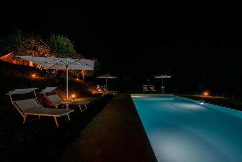 a swimming pool with chairs and an umbrella at night at La Maggiolina Country House in Montelabbate