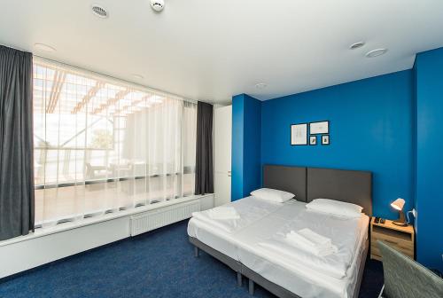 a bedroom with a bed with blue walls and a large window at Zaliakalnio terasos apartamentai in Kaunas