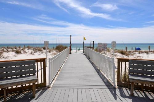 a wooden walkway to the beach with two benches at Pelican Beach Resort Destin in Destin