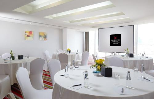 a room with white tables and white chairs and a screen at Millennium Central Downtown - Dubai in Dubai