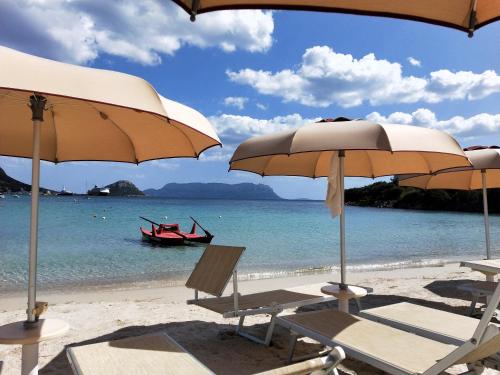 a beach with chairs and umbrellas and a boat in the water at Le stanze del mare in Golfo Aranci