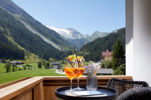 a table with two glasses on a balcony with a view at Adler Inn Tyrol Mountain Resort SUPERIOR in Tux