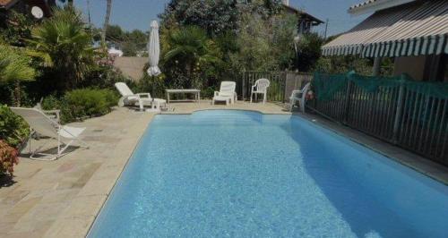 Una gran piscina azul con sillas y una mesa. en Villa Orion, en Capbreton