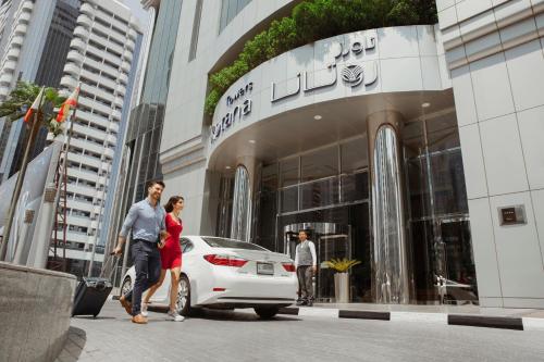 a man and woman walking past a white car in front of a building at Towers Rotana - Dubai in Dubai