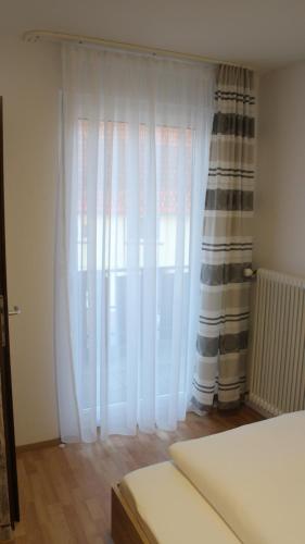 a bedroom with a large window with white curtains at Hotel Glas Schwarzwald in Fluorn