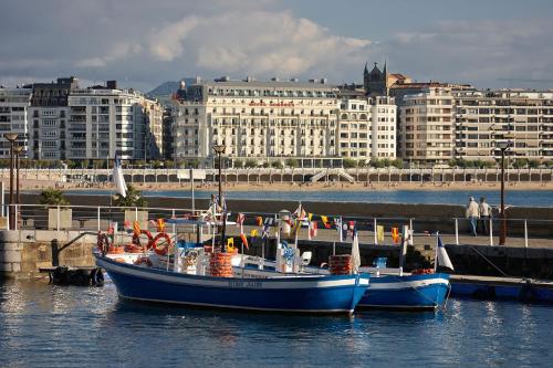 a blue boat is docked in the water near a city at ATeRIAN MUSKARIA in Zarautz
