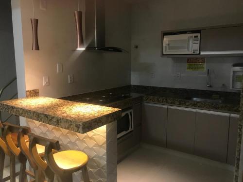 a kitchen with a counter with chairs and a microwave at Paradise Temporada Cobertura 4 Quartos com Jacuzzi e Churrasqueira no Thermas Paradise - Rio Quente in Rio Quente