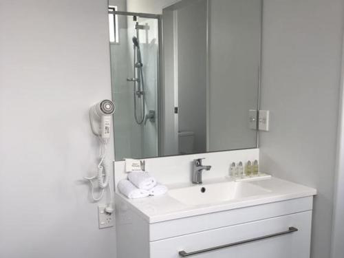 ein weißes Bad mit einem Waschbecken und einer Dusche in der Unterkunft Durham Court Motor Inn in Tauranga