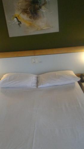 a bed with white sheets and a painting on the wall at Apart Hotel Quartier Latin in Vitória