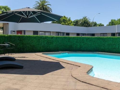 a swimming pool with an umbrella and a table and chairs at Durham Court Motor Inn in Tauranga