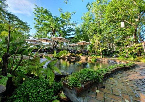a garden with a pond with umbrellas and trees at Anna-Nava Pakkret Hotel in Nonthaburi