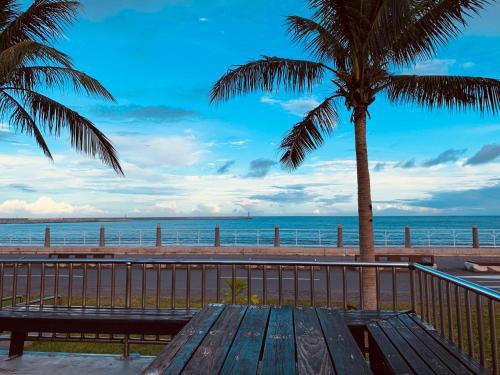 a wooden bench sitting next to a beach with a palm tree at Long To Sea Again in Hualien City