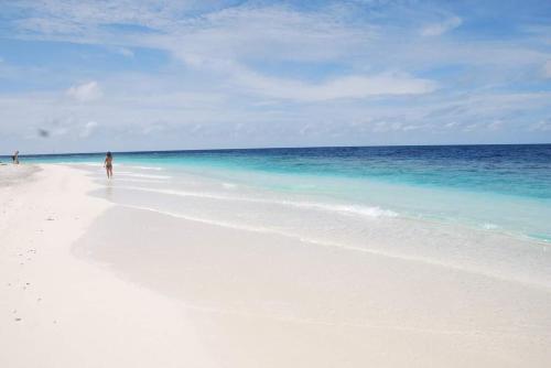 a person walking on a white beach with the ocean at Finimas Residence in Thimarafushi