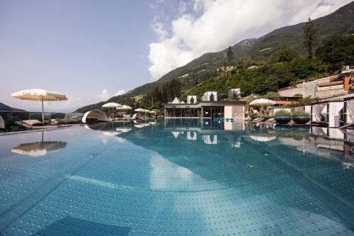 a large swimming pool with mountains in the background at Quellenhof Luxury Resort Passeier in San Martino