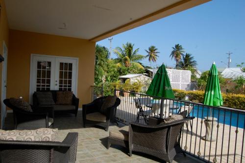 balkon z krzesłami, stołami i zielonymi parasolami w obiekcie Casa del Sol Tobago w mieście Bon Accord Village