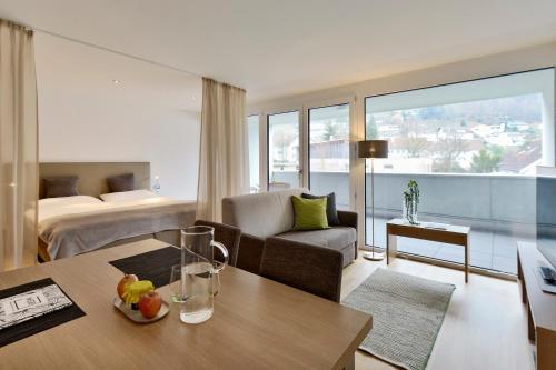 ein Wohnzimmer mit einem Sofa, einem Tisch und einem Bett in der Unterkunft Relaxed Urban Living - Aparthotel und Boardinghouse in Dornbirn