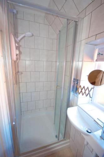 a shower with a glass door next to a sink at Wish Cottage in Ratton Village