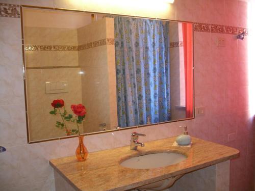 een wastafel in de badkamer met een spiegel en een vaas met rozen bij Affittacamere La Rosa in Lucca
