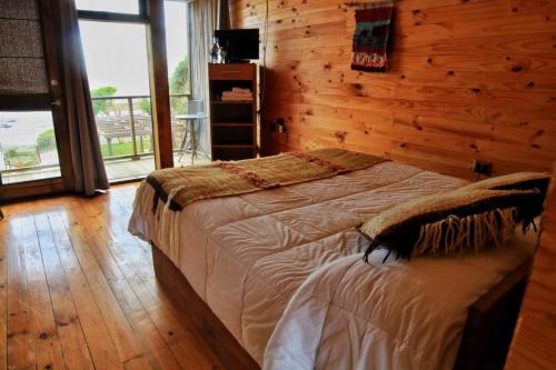 1 dormitorio con 1 cama y pared de madera en Ruka Antu Ecolodge en Cobquecura