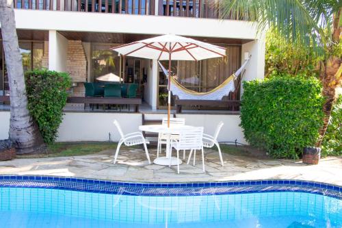 a table and chairs with an umbrella next to a pool at Nannai Residence Muro Alto in Porto De Galinhas