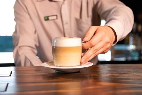 a man holding a cup of coffee on a table at ibis Styles Curitiba Aeroporto in São José dos Pinhais