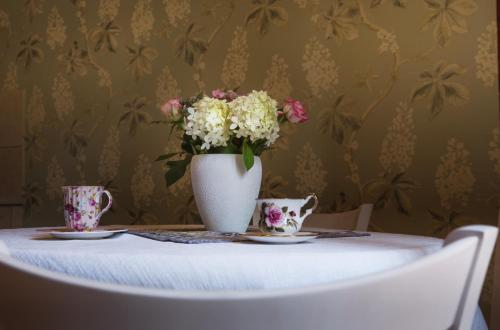 a vase of flowers sitting on a table with two cups at Leśny Ogród in Lanckorona
