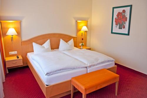 a bedroom with a large white bed and a orange stool at Hotel Rosenhof in Kerpen