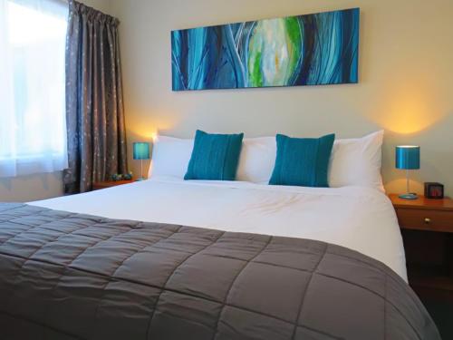 a bedroom with a large white bed with blue pillows at Almond Court Motel in Alexandra
