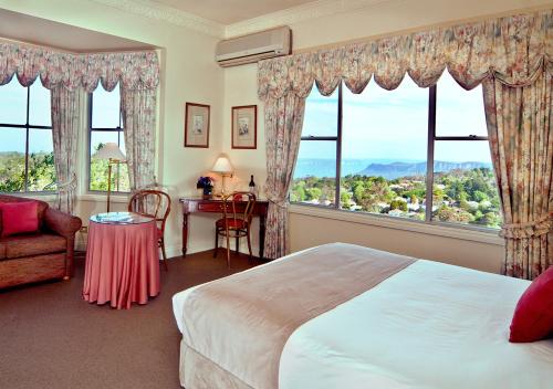 a bedroom with a bed and a desk and windows at Mountain Heritage Hotel in Katoomba