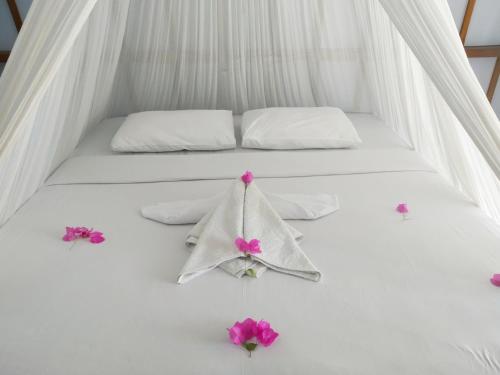 a bed with white sheets and pink flowers on it at Sunset Beach Bungalow in Gili Meno