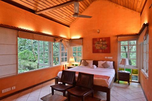 a bedroom with a bed and two chairs and windows at Mystic Mayapott, Thekkady in Thekkady