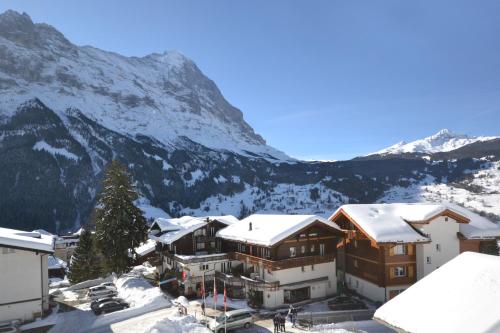 a building in the snow with mountains in the background at Hotel Caprice - Grindelwald in Grindelwald