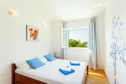 ein weißes Bett mit blauen Kissen in einem Zimmer mit Fenster in der Unterkunft Villa Maja Tucepi in Tučepi