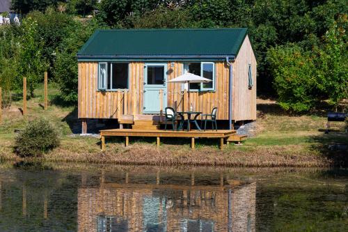 a wooden cabin with a table and an umbrella next to a lake at Lynstone Lakes in Bude