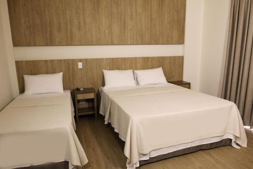 two beds in a hotel room with white sheets at Ouro Minas Plaza Hotel in Aparecida