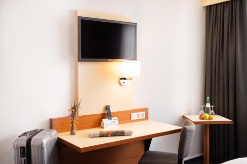 a hotel room with a desk with a television on the wall at Parkhotel Herne in Herne