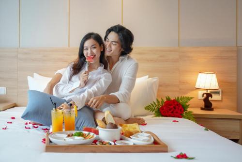 two women sitting on a bed with a tray of food at G8 Luxury Hotel and Spa Da Nang in Da Nang