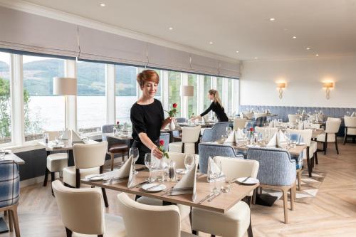 a woman standing in a dining room with tables and chairs at Loch Ness Clansman Hotel in Drumnadrochit