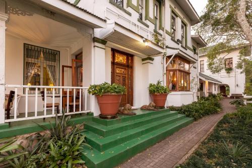 a white house with green steps and potted plants at Royston Hall Historical Guesthouse in Umtentweni
