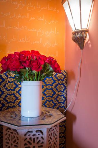 a vase of red roses on a table with a lamp at Riad Azoulay in Marrakech