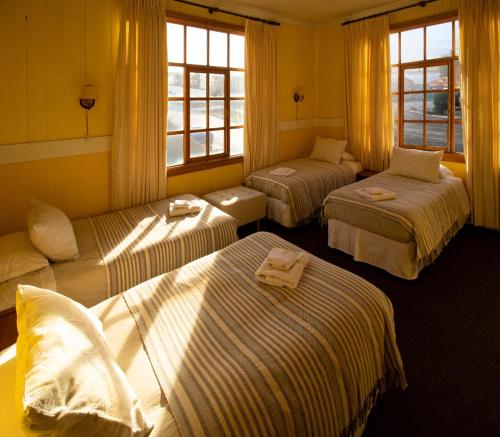 three beds in a room with yellow walls and windows at Yendegaia House in Porvenir