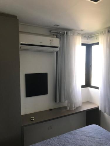 a bedroom with a tv and a bed and a window at Pajucara Flat in Maceió