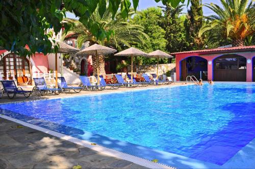 une grande piscine avec des chaises et des parasols bleus dans l'établissement Ilios Studios, à Pefki