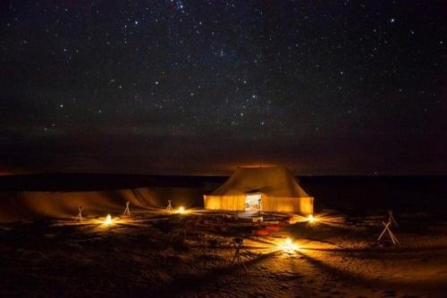 a yurt with lights on the beach at night at Erg Chegaga nomad tour in Mhamid