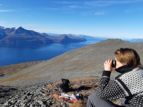 a woman sitting on top of a mountain talking on a cell phone at Lyngen Vista - Arctic Luxury in Hamnnes