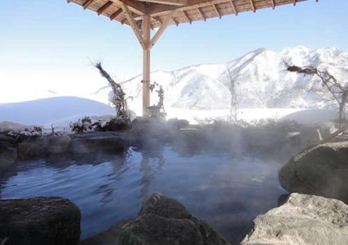 a hot tub with snow covered mountains in the background at Hotel Futaba in Yuzawa