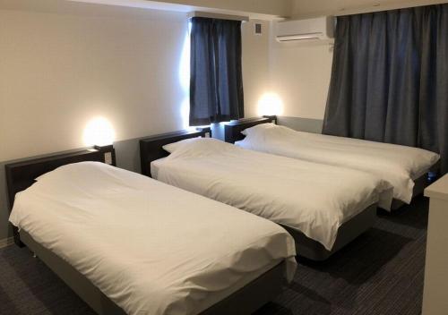 two beds in a hotel room with white sheets at Hotel Taiyo Nouen Furumitsu in Matsuyama
