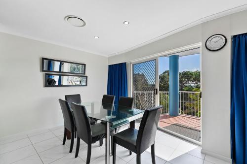 a dining room with a glass table and chairs and a balcony at White Crest Apartments in Hervey Bay