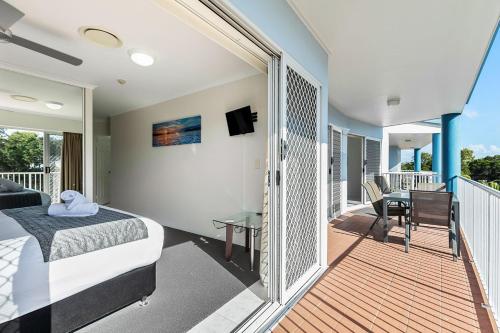 a bedroom with a balcony with a bed and a desk at White Crest Apartments in Hervey Bay