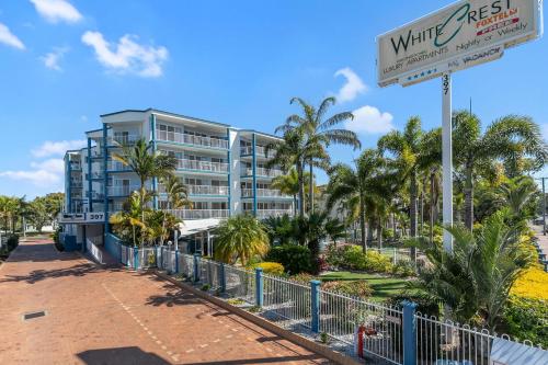 a sign in front of a building with palm trees at White Crest Apartments in Hervey Bay